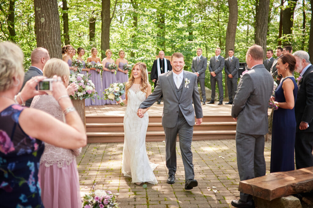 A newly married couple walks down the aisle following their outdoor wedding ceremony.