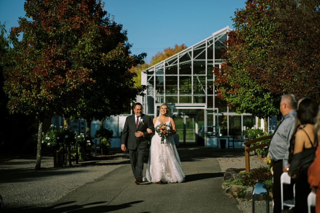A bride and her father walk down the aisle at her outdoor wedding on a beautiful fall day.