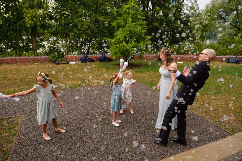 A couple celebrates their wedding ceremony while the flower girls blow bubbles at them.