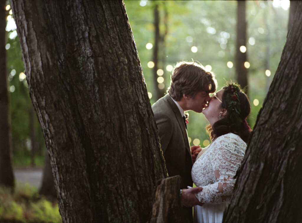 A couple kisses behind a tree after their wedding ceremony.