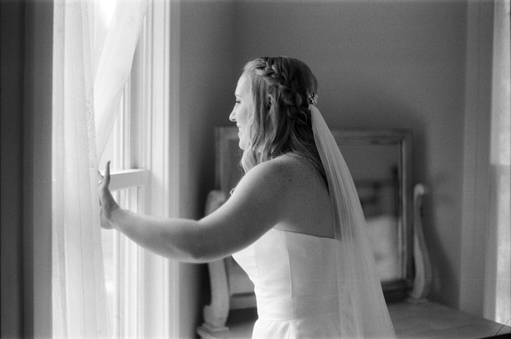 A bride looks out the window of her room at The Barn at Fallingwater, one of the best barn wedding venues in Pennsylvania. 