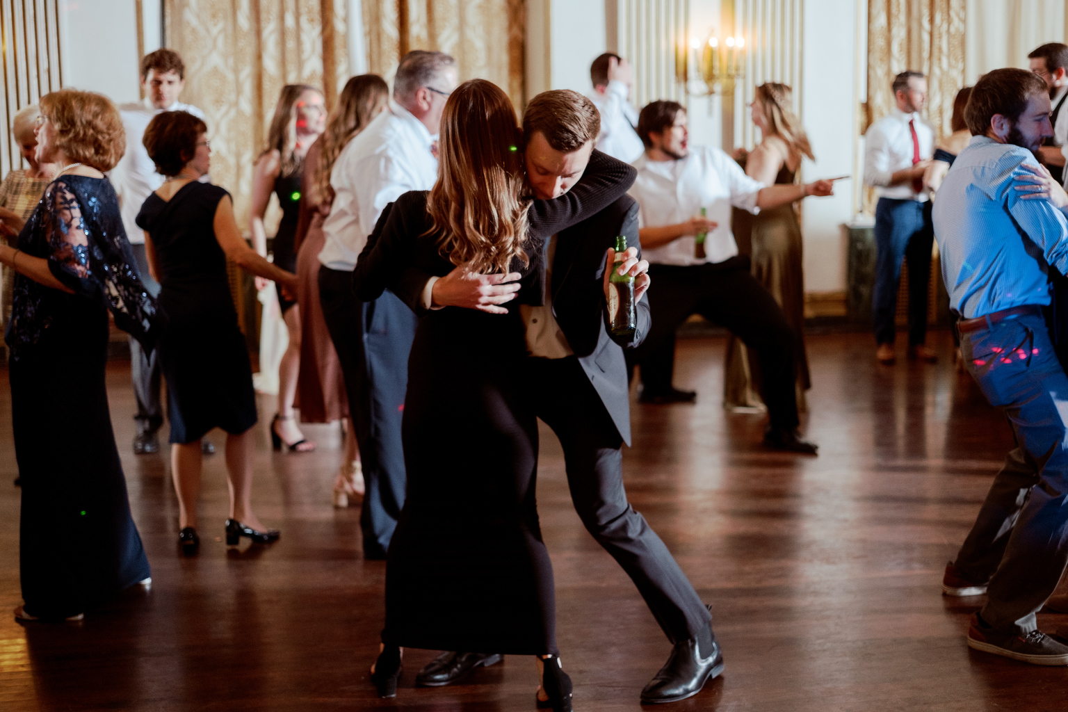 A couple dances at a wedding in an opulent room.